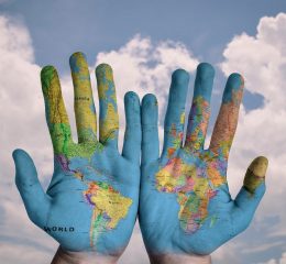 UCaP-The-Palms-Of-Hands-With-A-World-Map-Against-A-Blue-Sky-Background