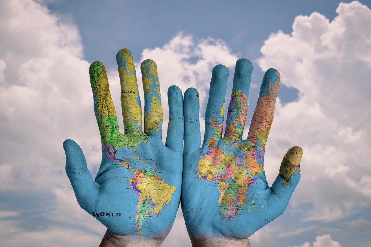 UCaP-The-Palms-Of-Hands-With-A-World-Map-Against-A-Blue-Sky-Background
